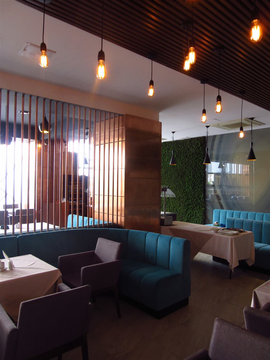 Sala restaurantului ziua, cu tavan din lamele de lemn și peretele din licheni în fundal