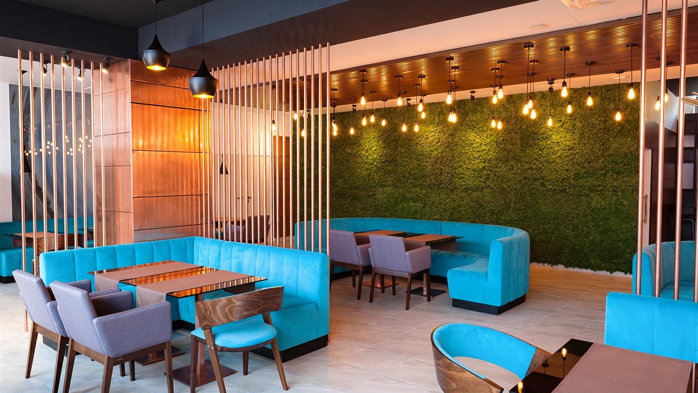 Restaurantul Premium Wellness Institute seara, cu perete din licheni stabilizați, banchete turcoaz și becuri Edison
