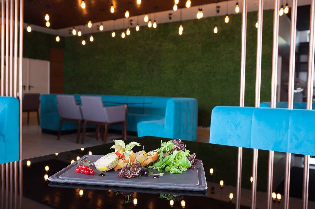 Masă servită în restaurantul Premium Wellness Institute, cu peretele din licheni stabilizați, banchete turcoaz și becuri Edison în fundal